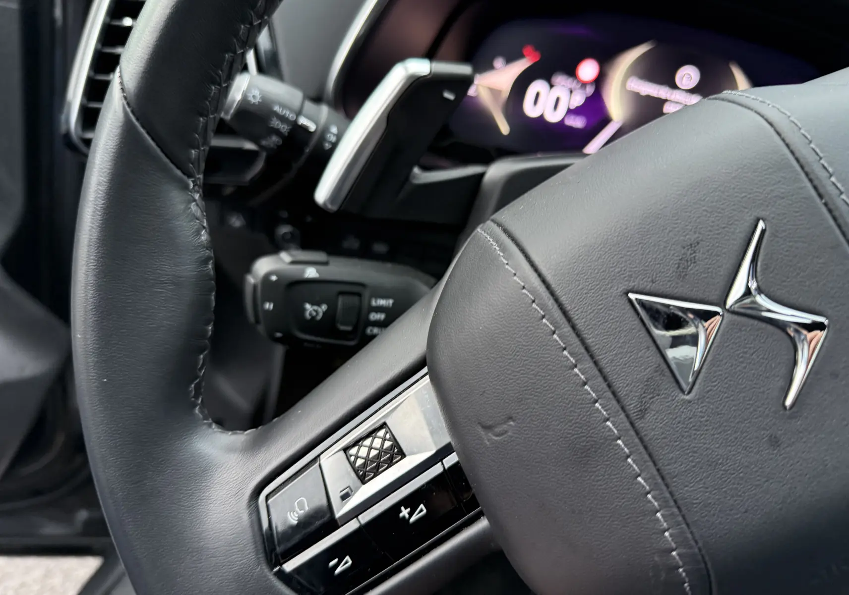 Gros plan sur le volant en cuir noir du DS7 BlueHDi 130 2025 avec commandes intégrées et tableau de bord numérique flou.