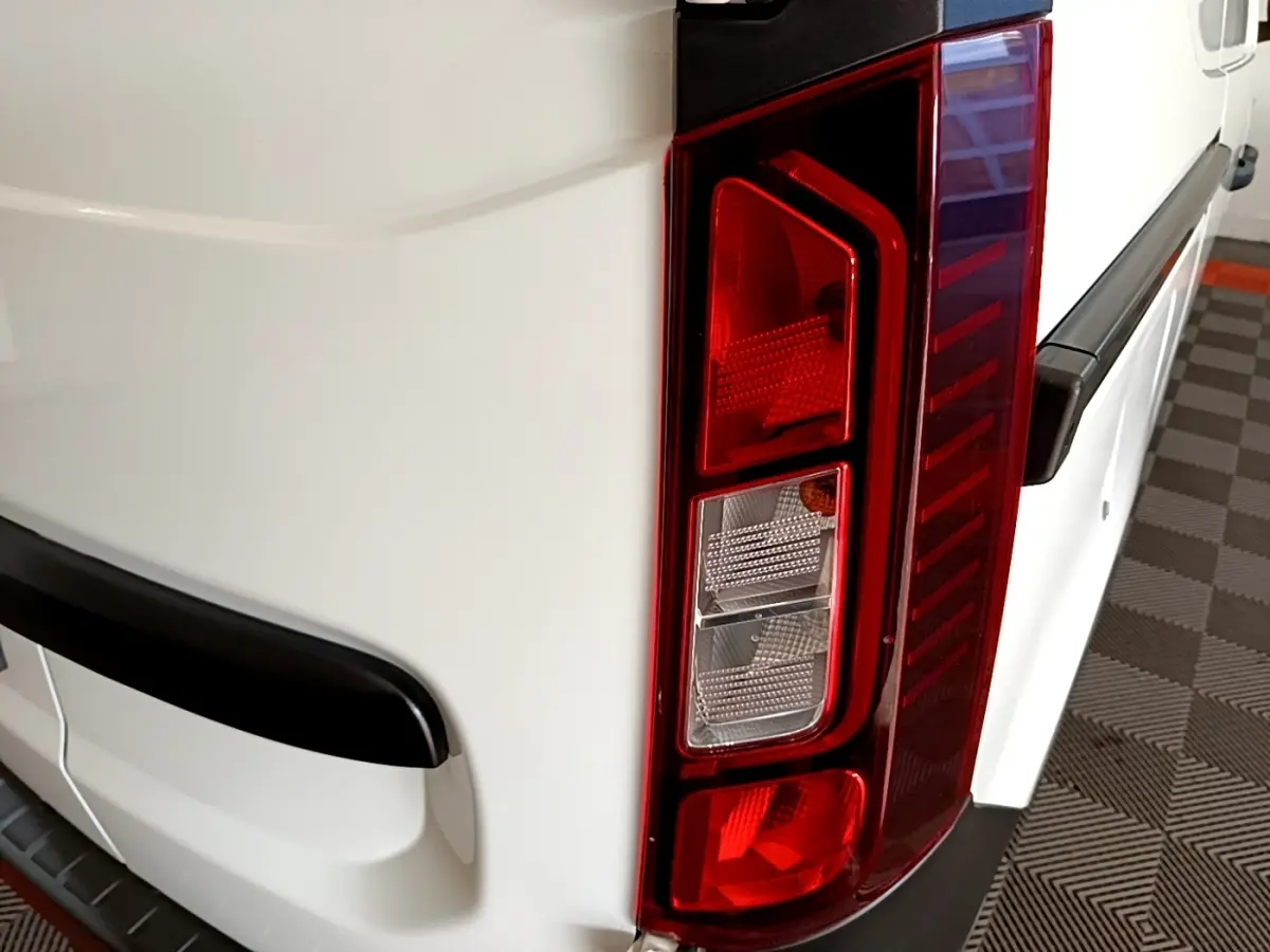 Gros plan sur le feu arrière droit d’un Renault Express blanc, avec pare-chocs noir et surface lisse du véhicule.