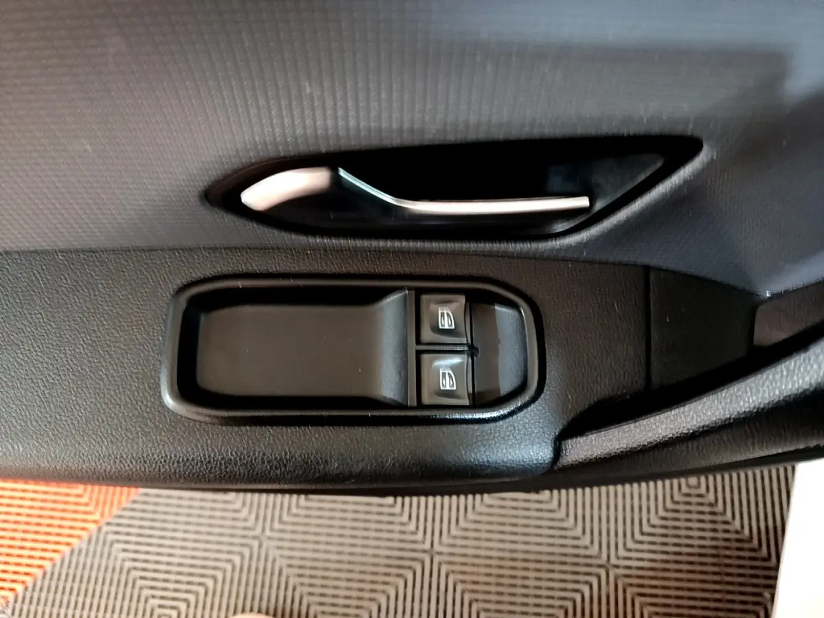 Poignée de porte intérieure noire avec commandes des vitres électriques sur Renault Express blanc, vue de profil côté conducteur.