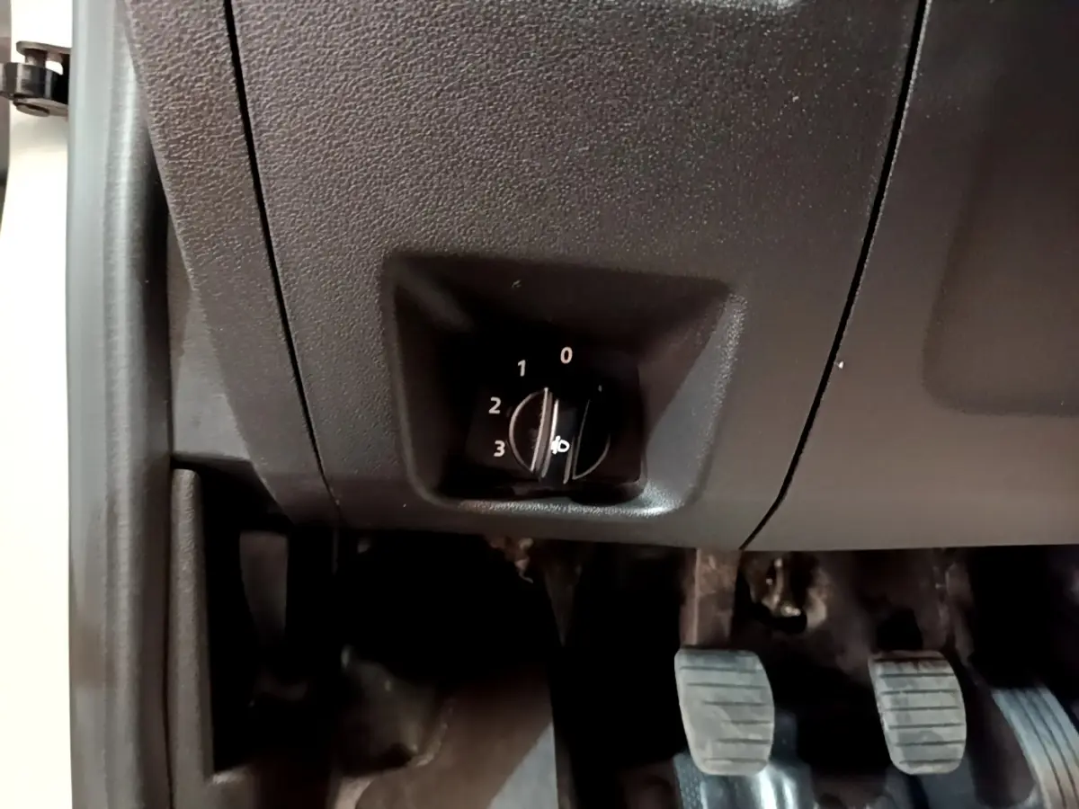 Détail du réglage manuel des phares dans l'habitacle d'un Renault Express blanc, vue côté conducteur vers les pédales.