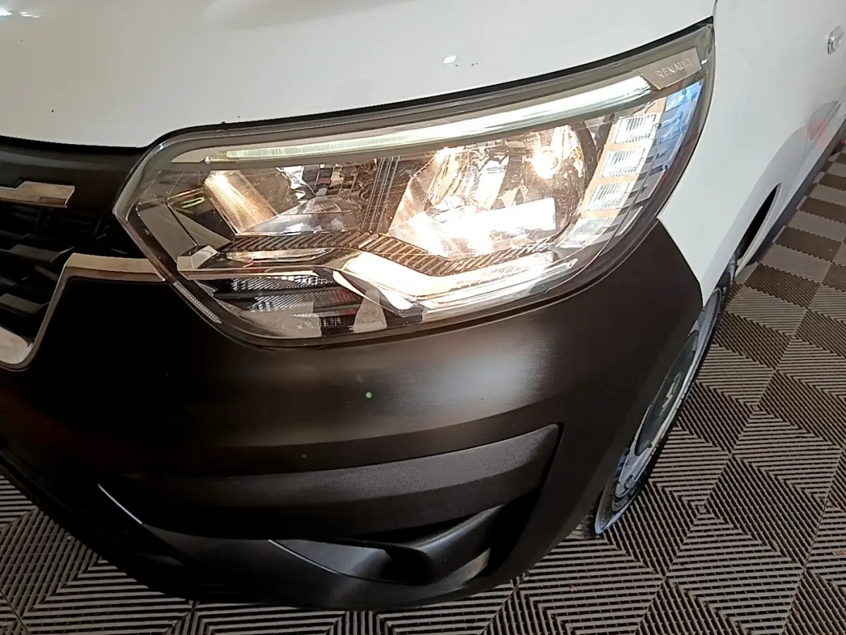 Gros plan sur le phare avant droit allumé d’un Renault Express blanc avec pare-chocs noir mat.