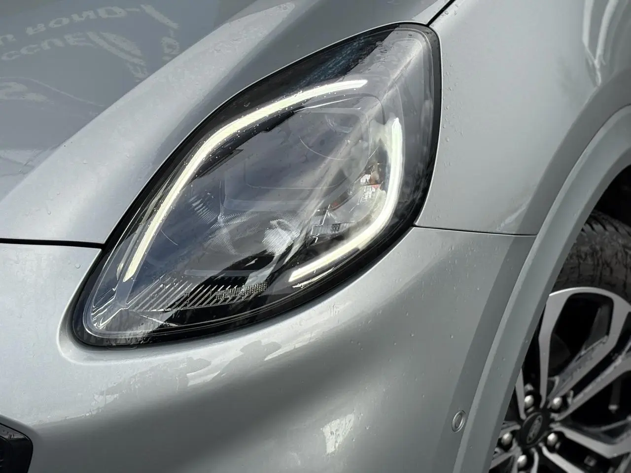 Gros plan sur le phare avant gauche allumé du Ford Puma gris Solar avec jante alliage visible et carrosserie brillante.