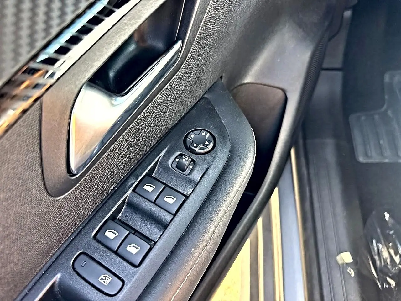 Gros plan sur la commande des vitres électriques côté gauche de la porte avant d’une Peugeot 208 gris artense.