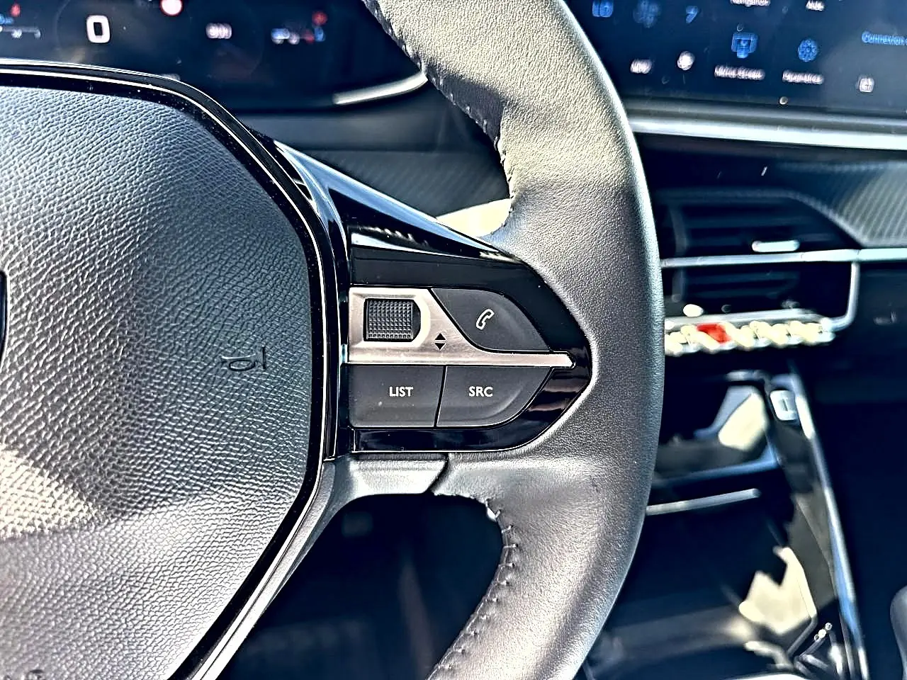 Gros plan sur le volant cuir noir côté gauche de la Peugeot 208 1.2 100 Allure avec commandes audio intégrées.