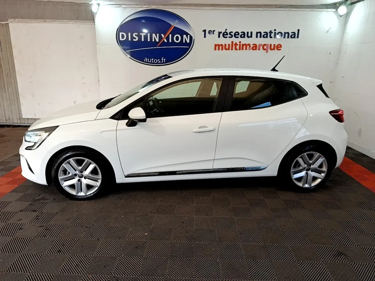 Profil droit d'une Renault Clio Business Blue dCi 115 blanche, avec jantes alliage et vitres teintées, en intérieur showroom.