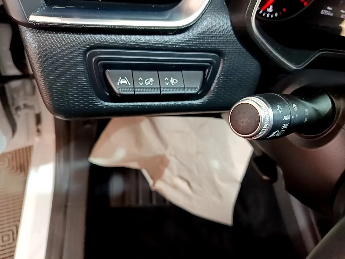 Gros plan sur les commandes d'assistance à la conduite et réglage des phares à gauche du volant dans une Renault Clio blanche 2020.