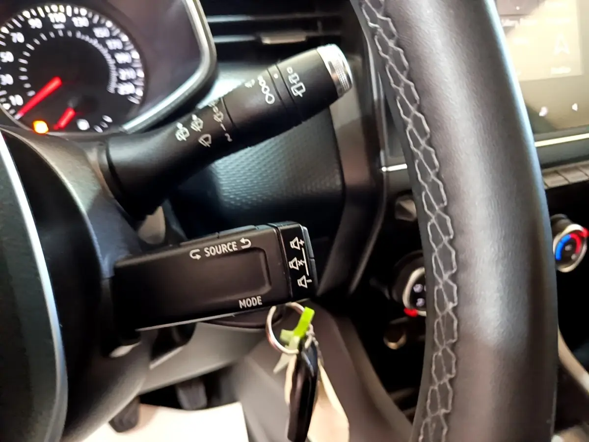 Gros plan sur le volant noir et la commande multimédia à gauche du tableau de bord intérieur d’une Renault Clio blanche.