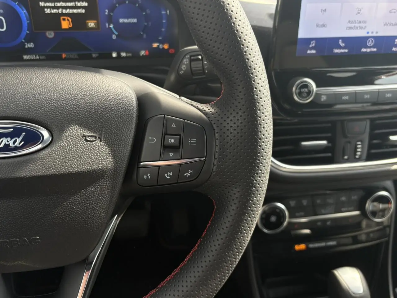 Gros plan sur le volant perforé noir avec surpiqûres rouges et tableau de bord numérique du Ford Puma Ecoboost 2023.