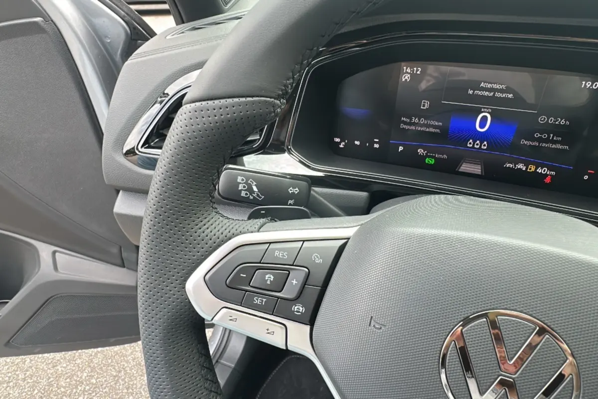 Gros plan sur le volant cuir perforé et le tableau de bord digital du Volkswagen T-Roc gris pyrite, version R-Line Black.