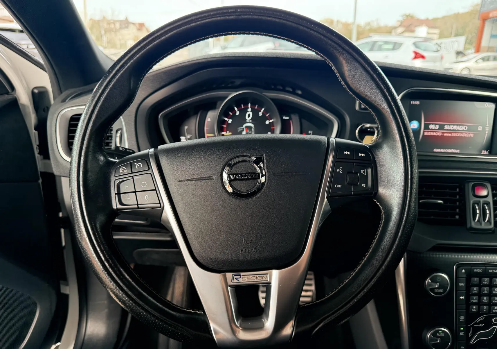 Vue rapprochée du volant noir R-Design d'une Volvo V40 blanche de 2017, avec tableau de bord et écran central visibles.