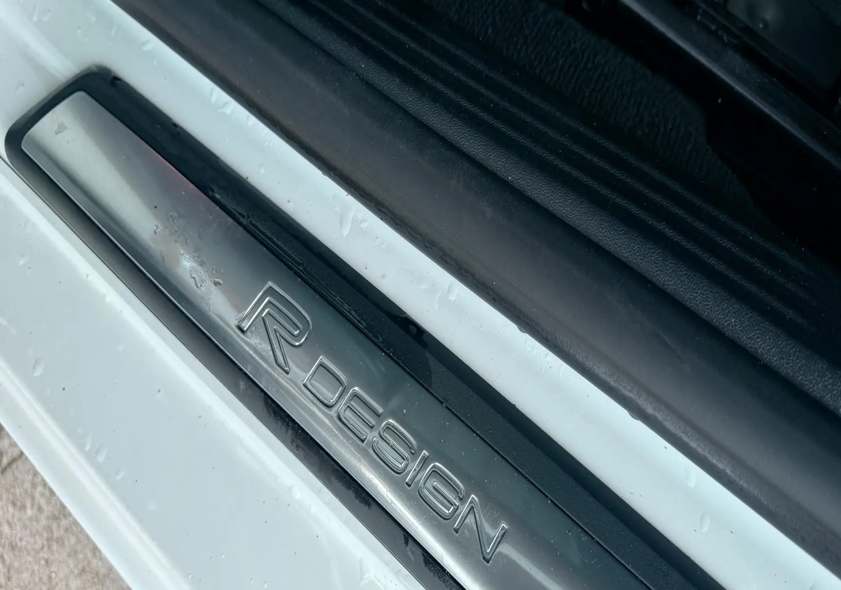 Gros plan sur la plaque de seuil de porte R-Design d'une Volvo V40 blanche, côté gauche, avec traces d'eau.