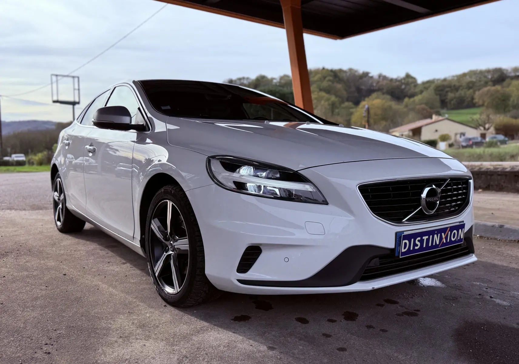 Vue 3/4 avant gauche d'une Volvo V40 R-Design blanche de 2017 avec jantes alliage et calandre noire distinctive.