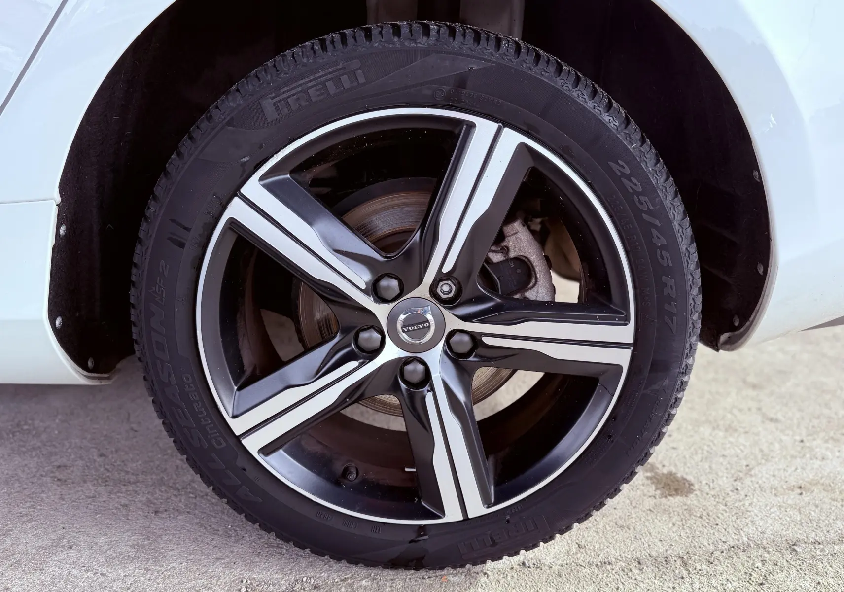 Gros plan sur la roue avant droite d'une Volvo V40 blanche, jante alliage R-Design à cinq branches noires et argentées.