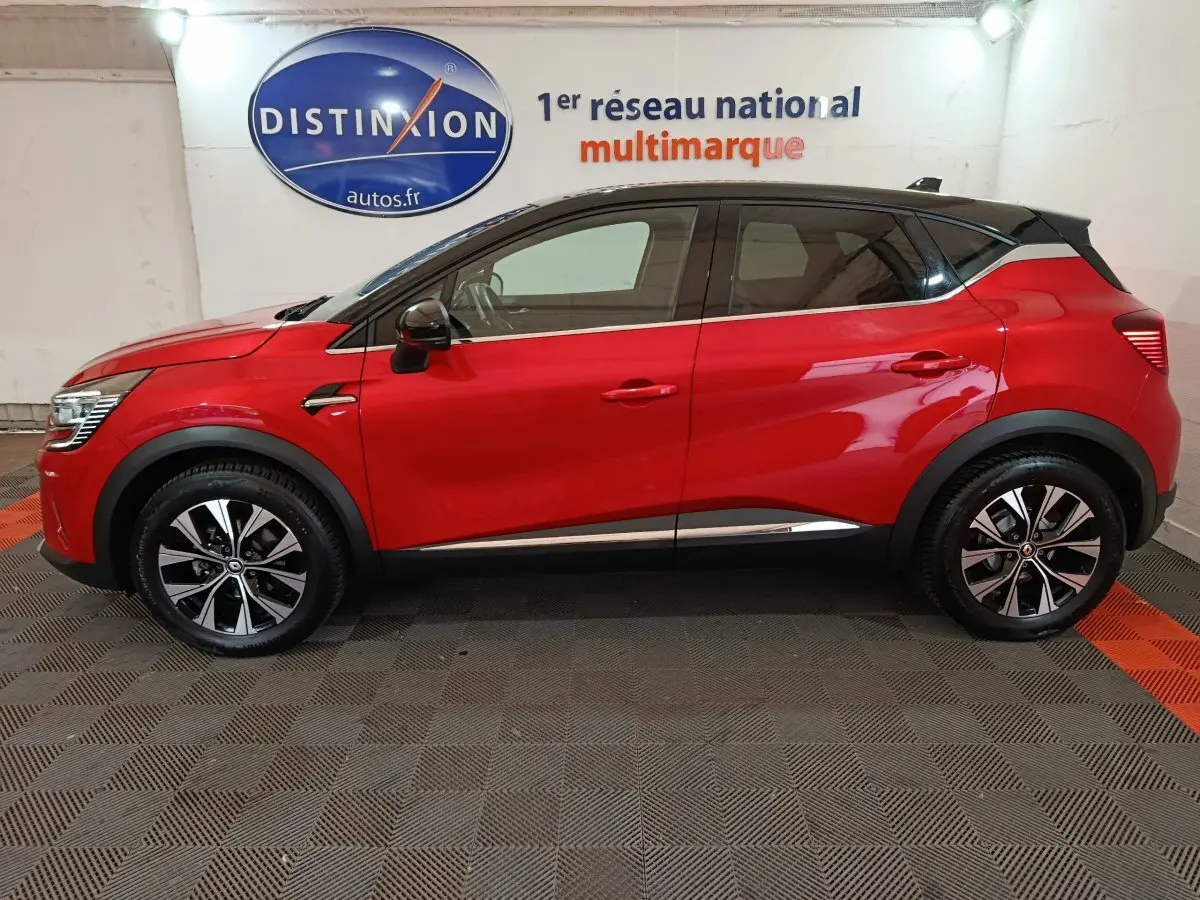 Vue latérale droite d'un Renault Captur Techno TCe 90 rouge avec toit noir et jantes alliage bicolores.