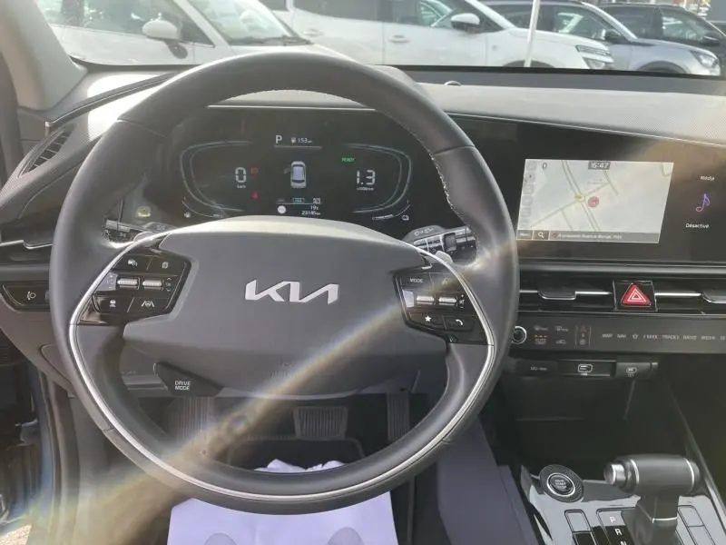 Vue intérieure centrée sur le volant KIA d’un Niro bleu métal 2024, avec tableau de bord digital et écran tactile de navigation.