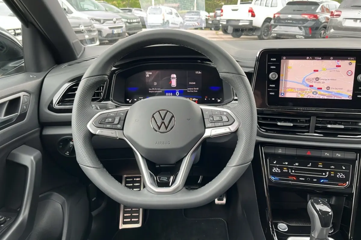 Vue intérieure centrée sur le volant cuir multifonctions du Volkswagen T-Roc gris indium avec tableau de bord digital.