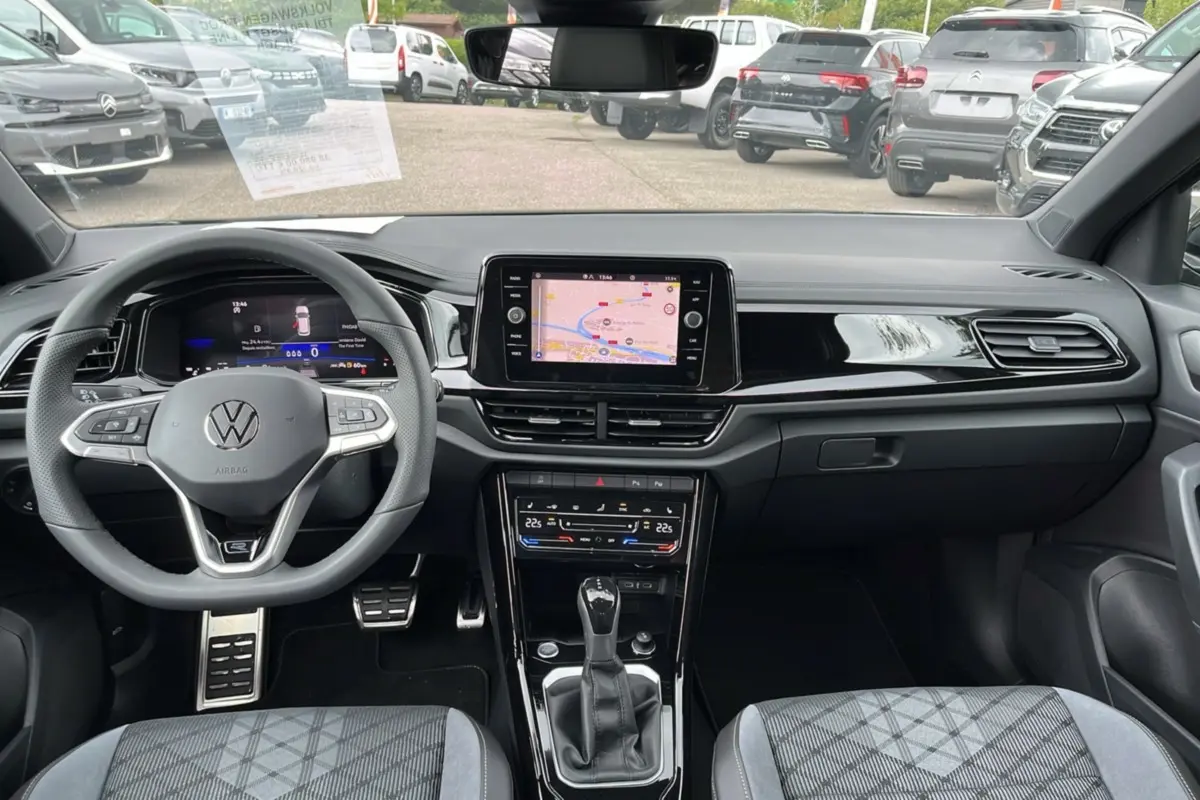 Vue intérieure avant du Volkswagen T-Roc gris indium, avec tableau de bord numérique et écran tactile central affichant la navigation GPS.