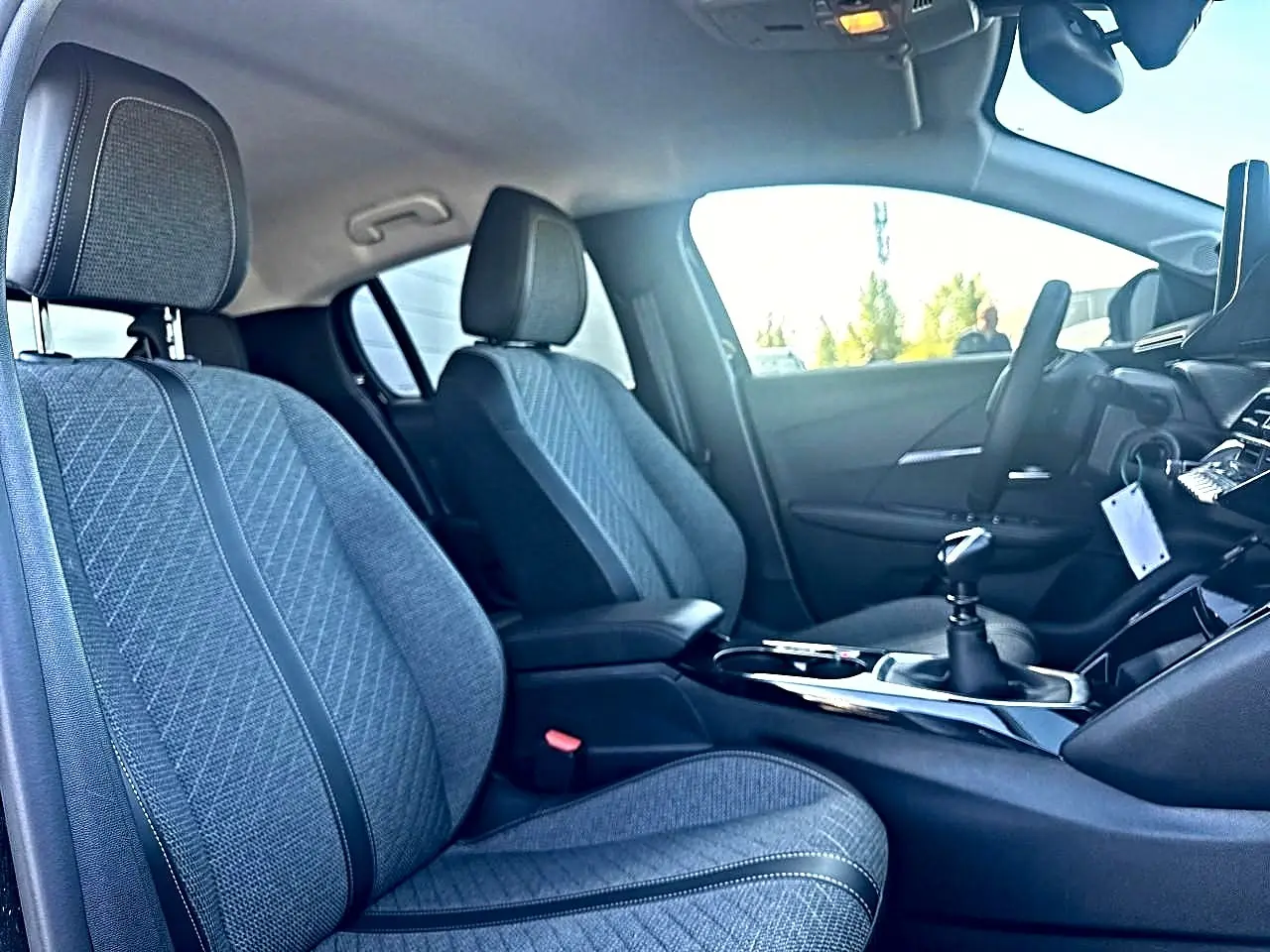 Intérieur de la Peugeot 208 1.2 100 Allure 2025, vue côté droit sur les sièges tissu gris et la boîte manuelle.
