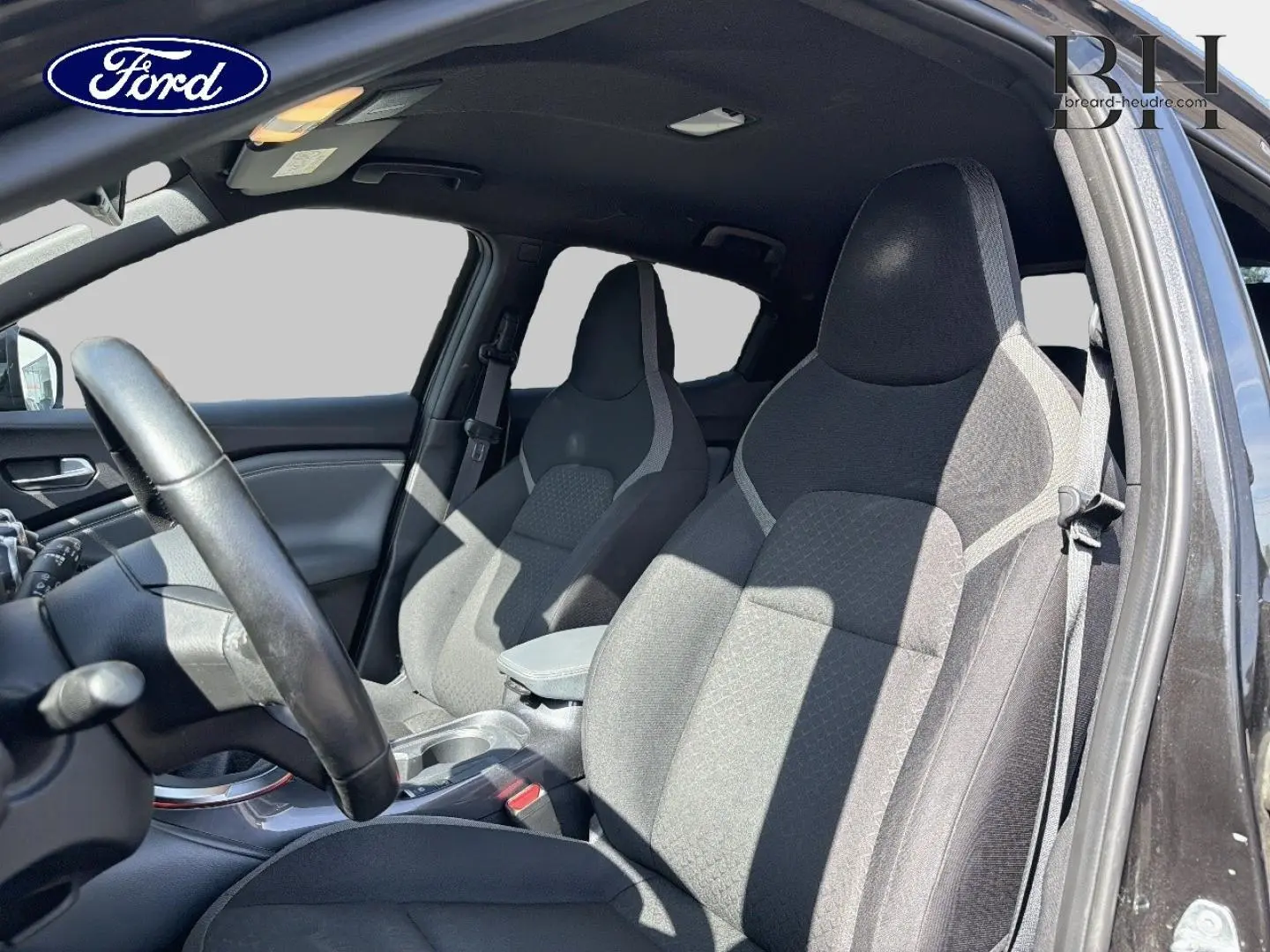 Vue intérieure côté conducteur du Nissan Juke 2020 noir métallisé, mettant en valeur les sièges avant en tissu gris foncé.
