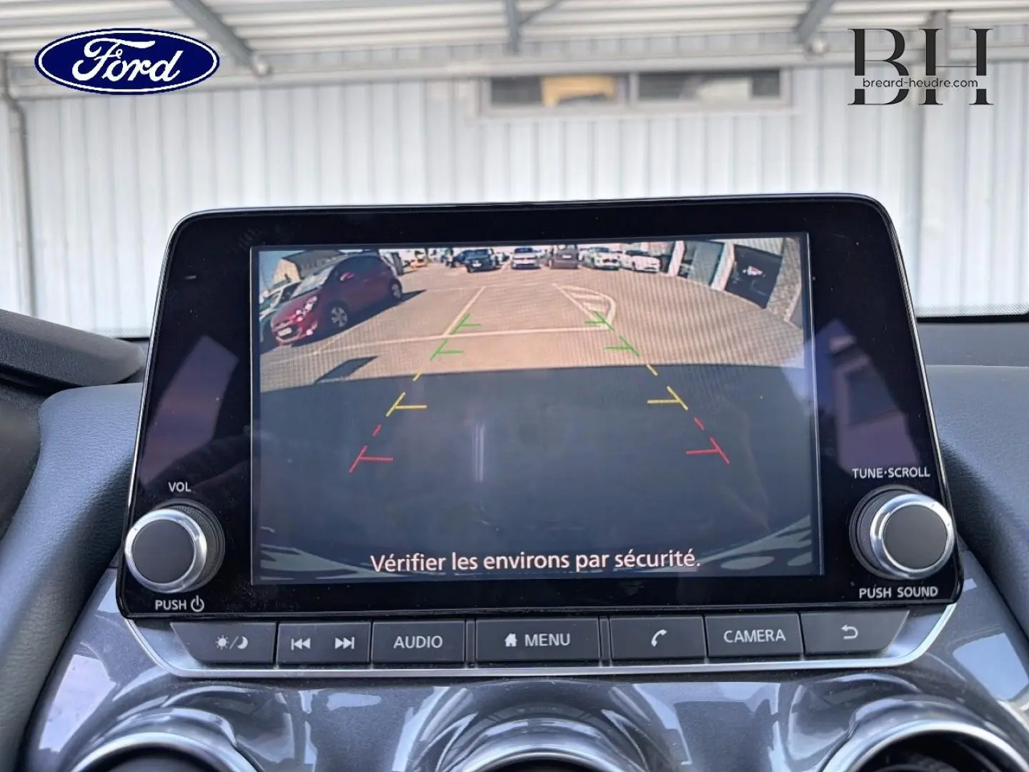 Écran tactile intérieur montrant la caméra de recul d'une Nissan Juke noir métallisé, avec commandes audio visibles.