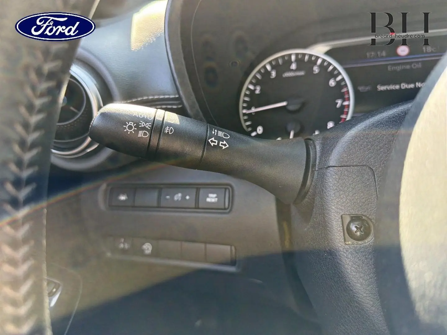 Gros plan sur la manette de clignotants noire à gauche du volant dans l'habitacle d'une Nissan Juke noir métallisé.