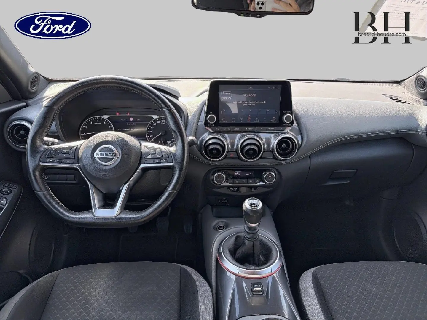 Vue intérieure avant du Nissan Juke 2020 avec volant cuir multifonction et écran tactile central, levier de vitesse manuel visible.