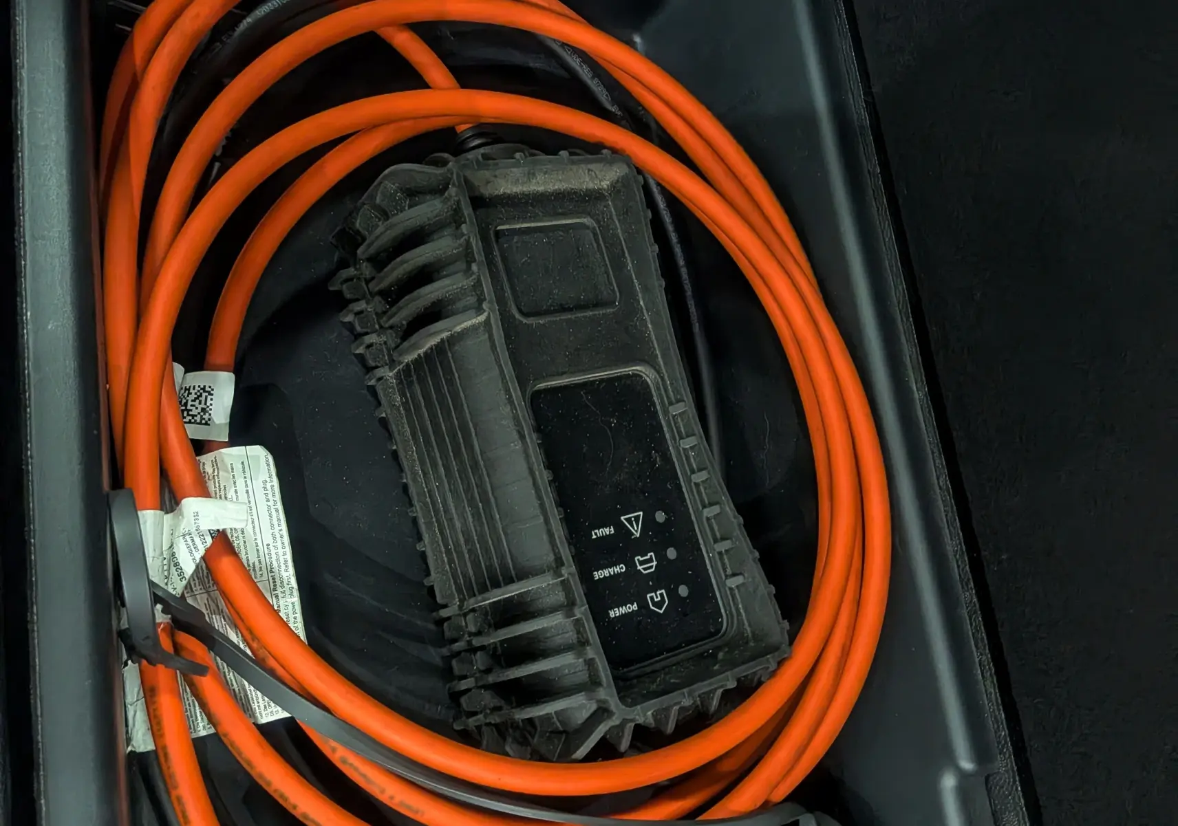 Gros plan sur le câble de recharge orange du Citroën C5 Aircross Hybride Rechargeable blanc, rangé dans son compartiment intérieur.