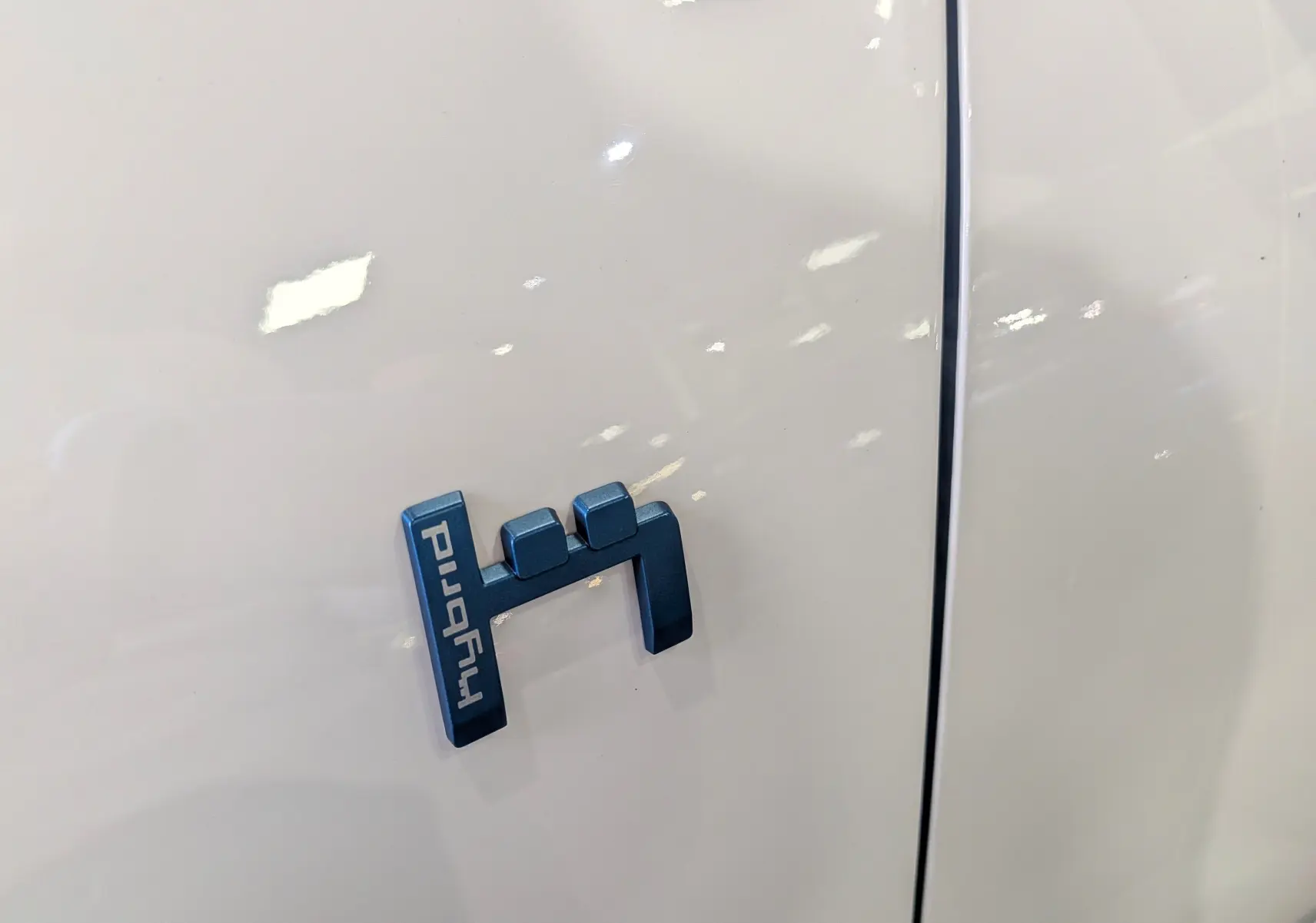 Gros plan sur l'insigne "hybrid" bleu sur la carrosserie blanche glacée d'une Citroën C5 Aircross hybride rechargeable.
