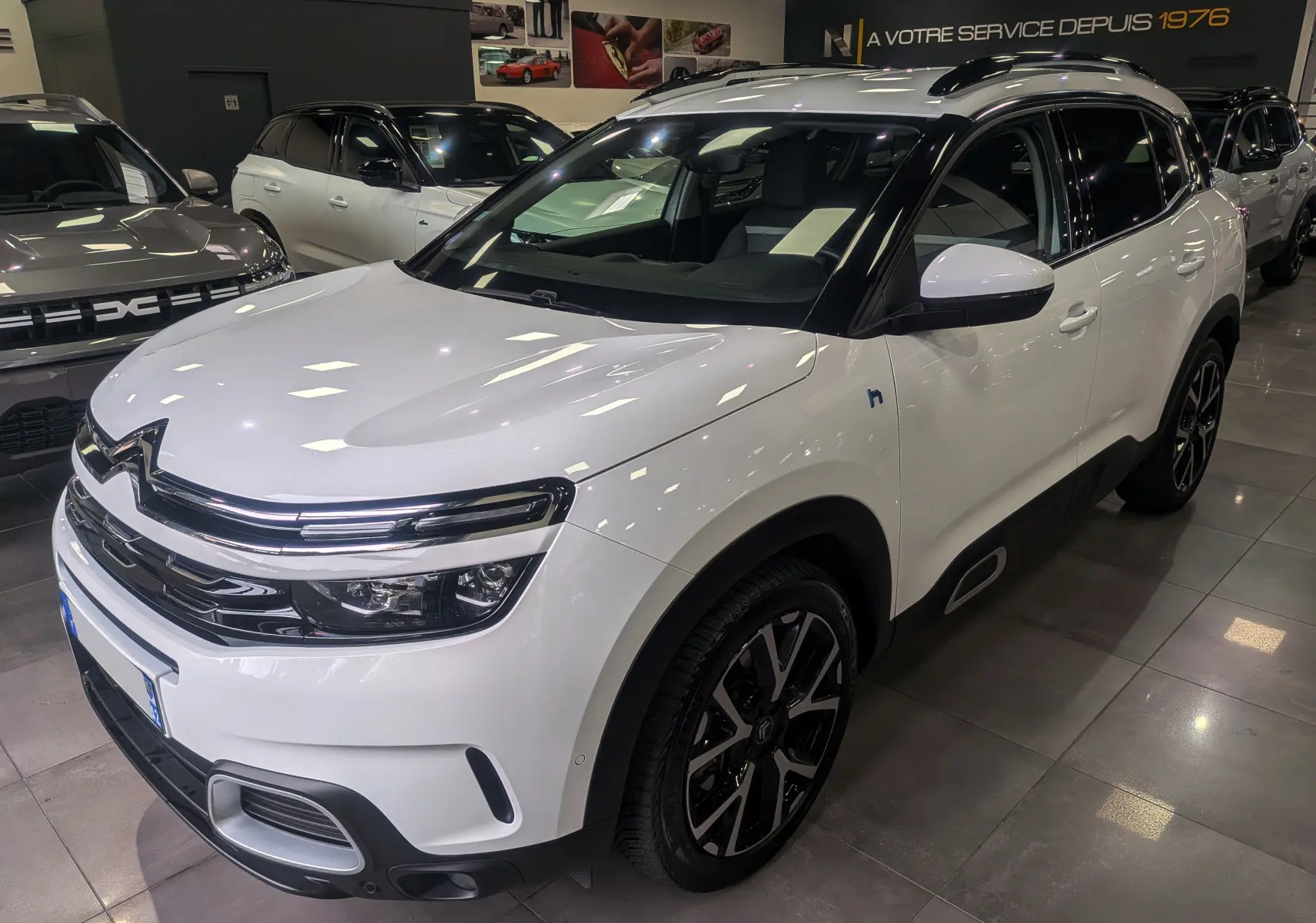 Vue 3/4 avant d'un Citroën C5 Aircross blanc glacier hybride rechargeable avec jantes noires et toit noir en showroom.
