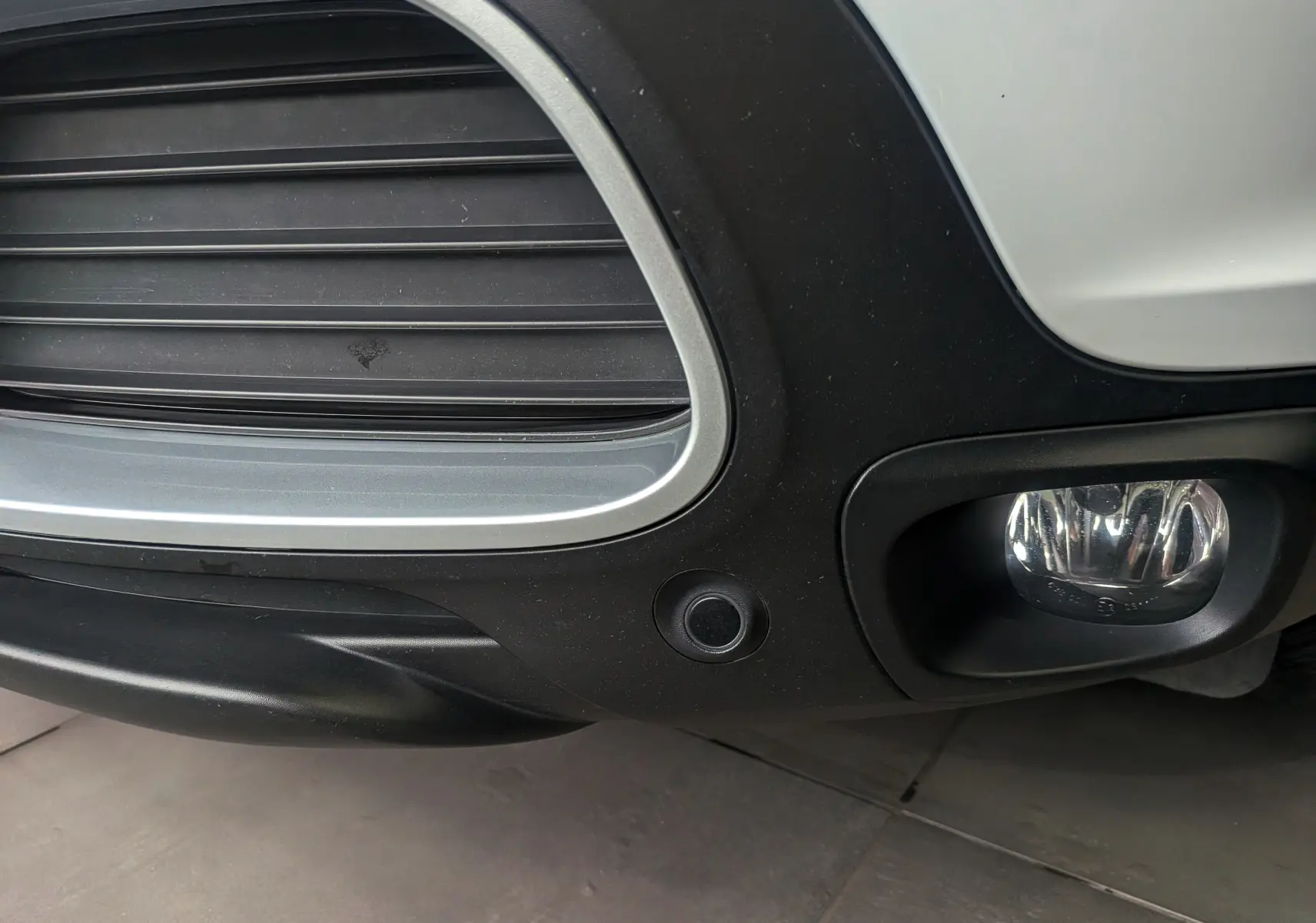 Gros plan sur le pare-chocs avant droit blanc glacier du Citroën C5 Aircross hybride avec antibrouillard et capteur de stationnement.