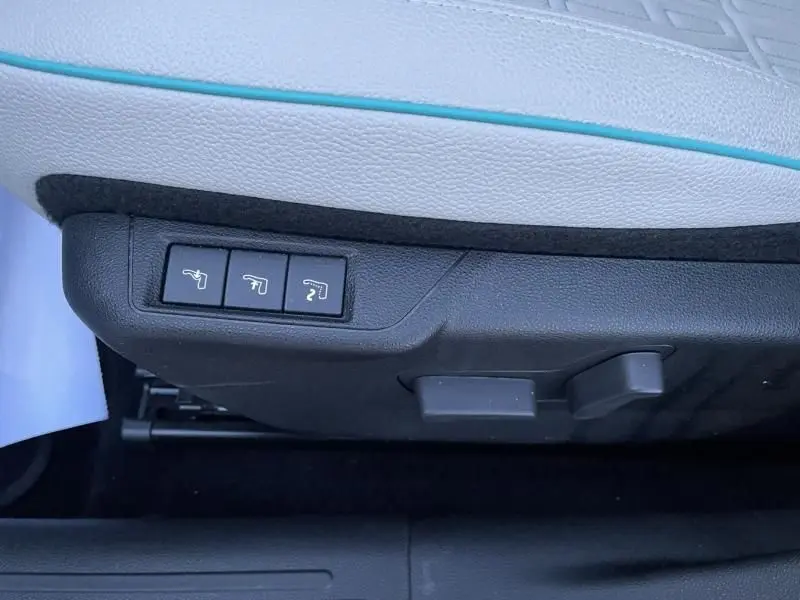 Détail des commandes de réglage électrique du siège côté gauche, avec sellerie blanche et surpiqûres bleues du FIAT 600 hybride 2025.