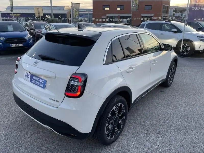 Vue 3/4 arrière droite d'une Fiat 600 blanche hybride 2025 avec feux arrière LED et jantes noires distinctives.