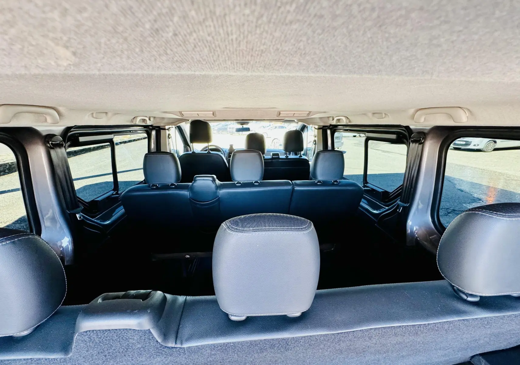 Vue intérieure arrière du Nissan NV300 Combi gris, montrant les sièges en tissu noir sur trois rangées.