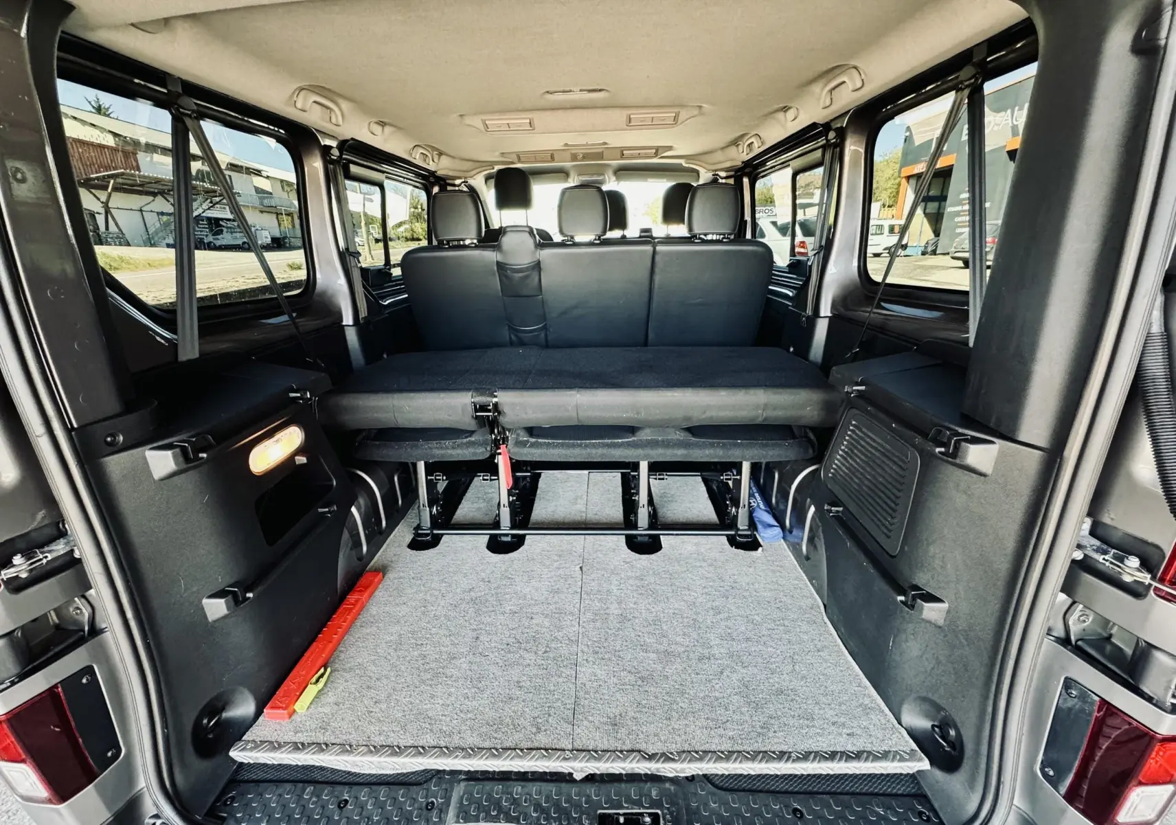 Vue arrière de l’intérieur gris et noir du Nissan NV300 Combi 9 places avec banquette rabattue et espace de chargement.
