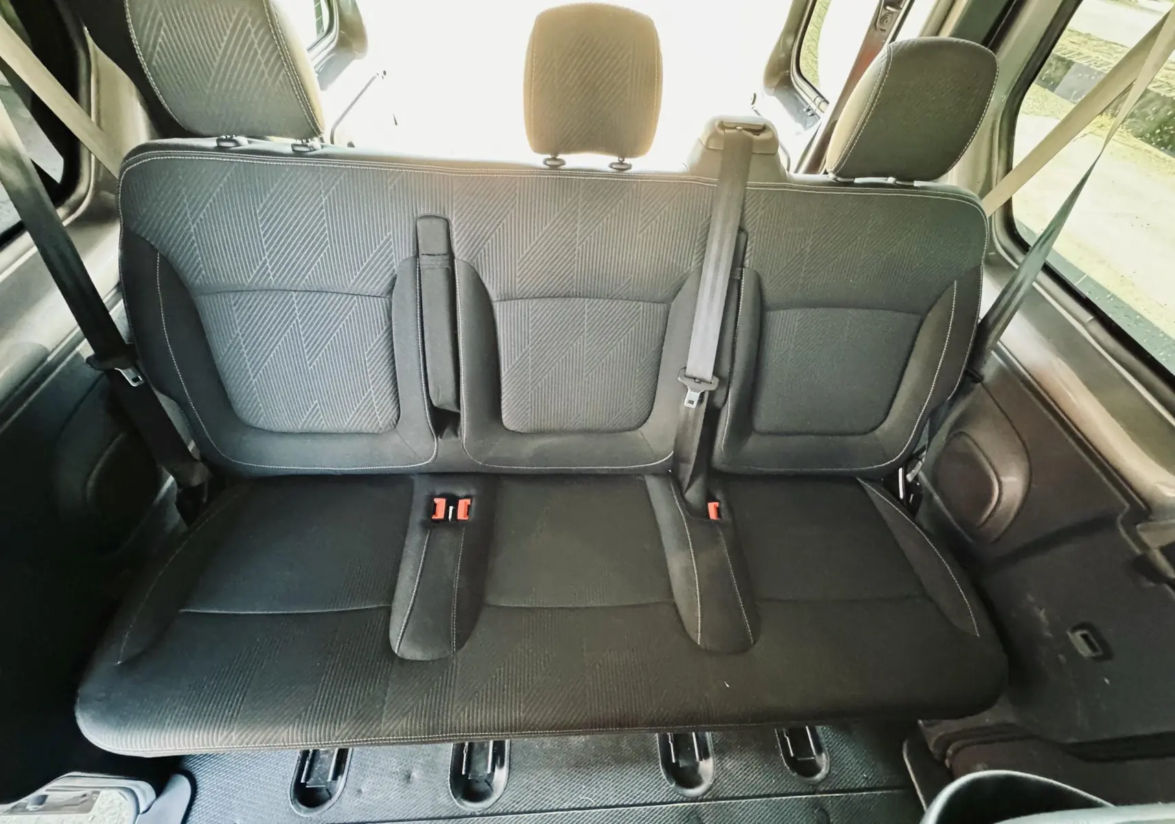 Vue intérieure arrière des sièges en tissu gris foncé du Nissan NV300 Combi, avec ceintures de sécurité visibles.