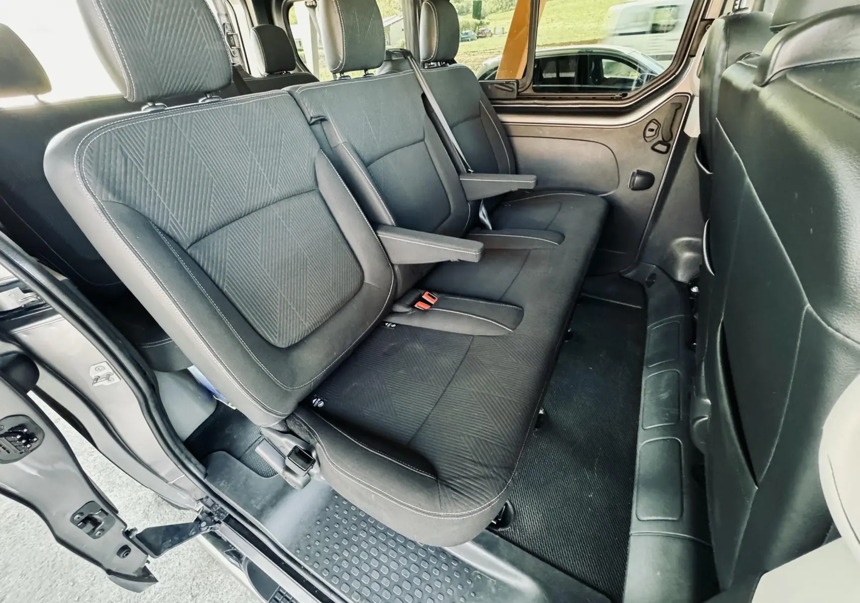 Vue intérieure côté gauche montrant la banquette arrière noire du Nissan NV300 Combi gris avec accoudoirs rabattables.