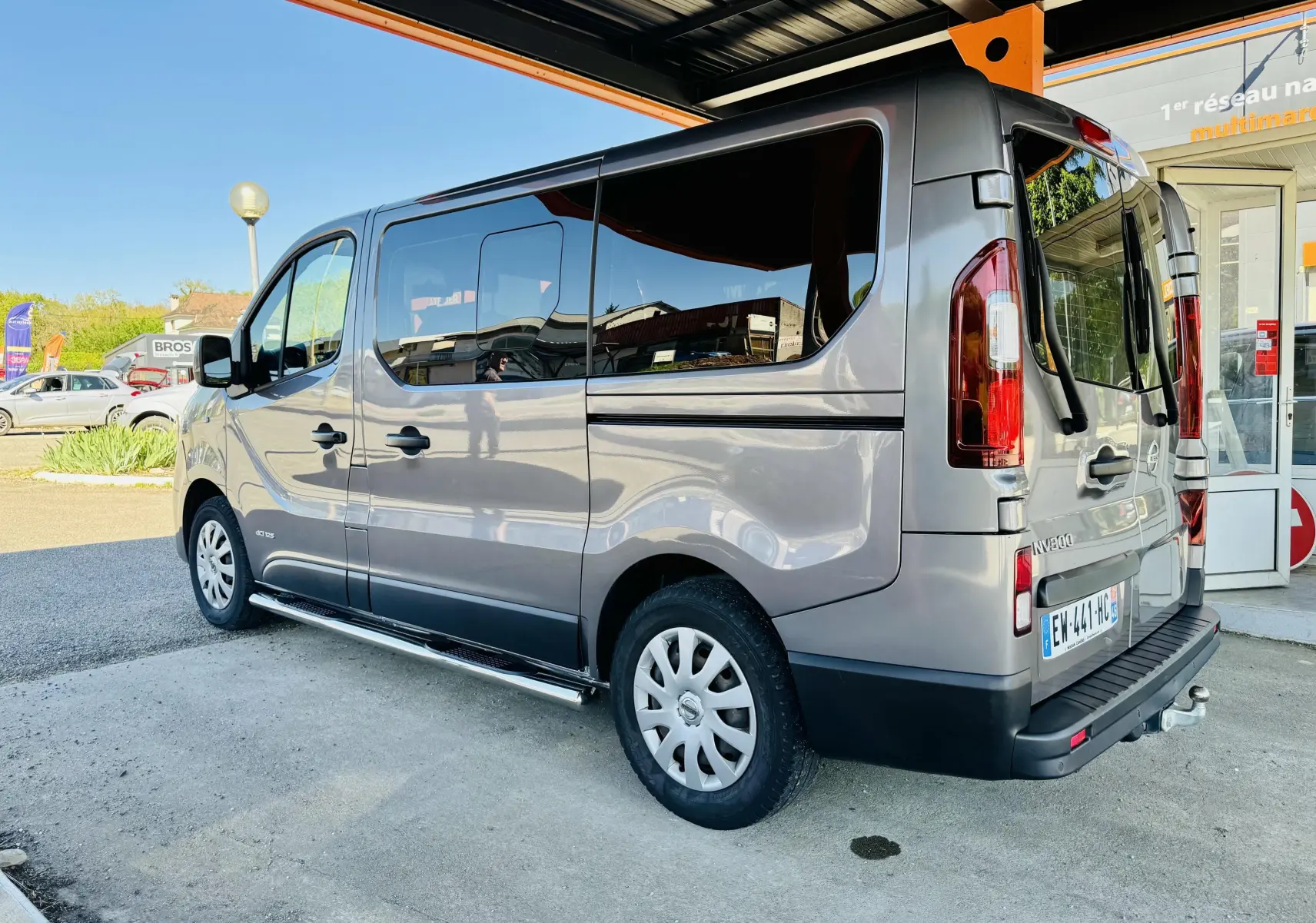 Vue 3/4 arrière droite d’un Nissan NV300 Combi gris avec vitres teintées et marchepied latéral.