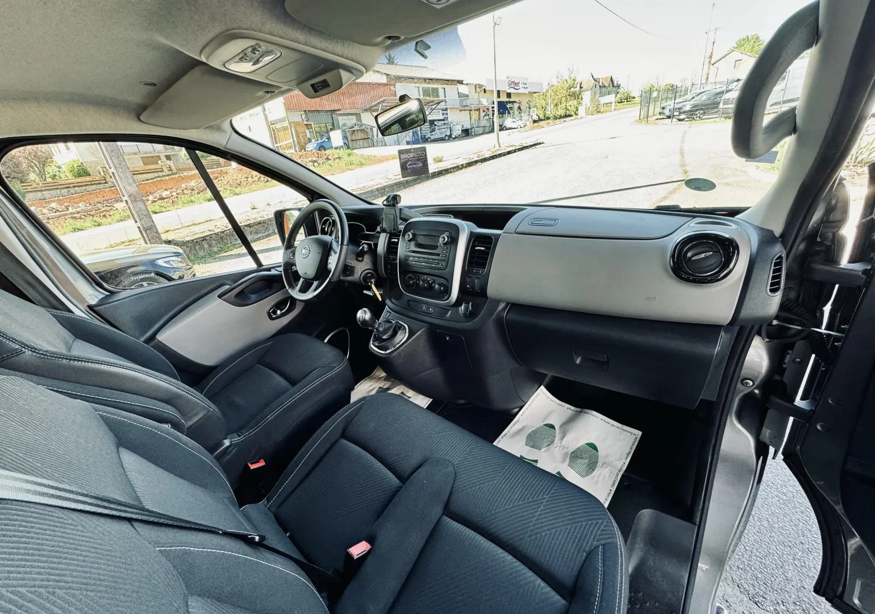 Vue intérieure côté conducteur du Nissan NV300 Combi gris, montrant le tableau de bord et les sièges en tissu noir.