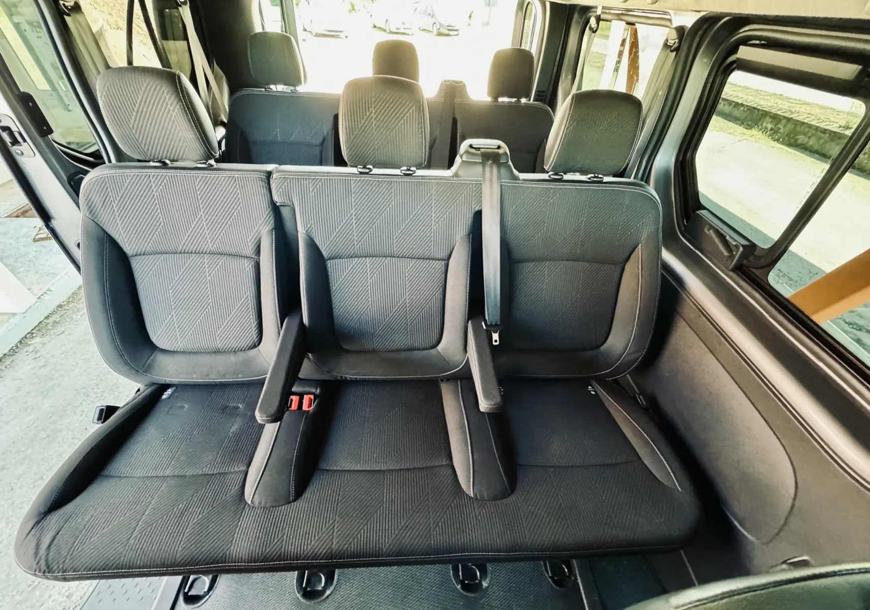 Vue intérieure arrière montrant les sièges en tissu gris du Nissan NV300 Combi 9 places, avec ceintures et appuie-têtes visibles.