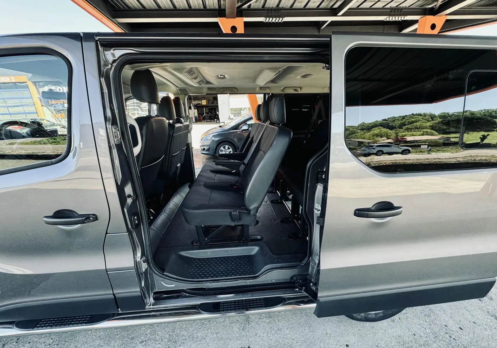 Vue latérale droite d’un Nissan NV300 Combi gris 2018 avec porte coulissante ouverte montrant les sièges passagers en tissu noir.