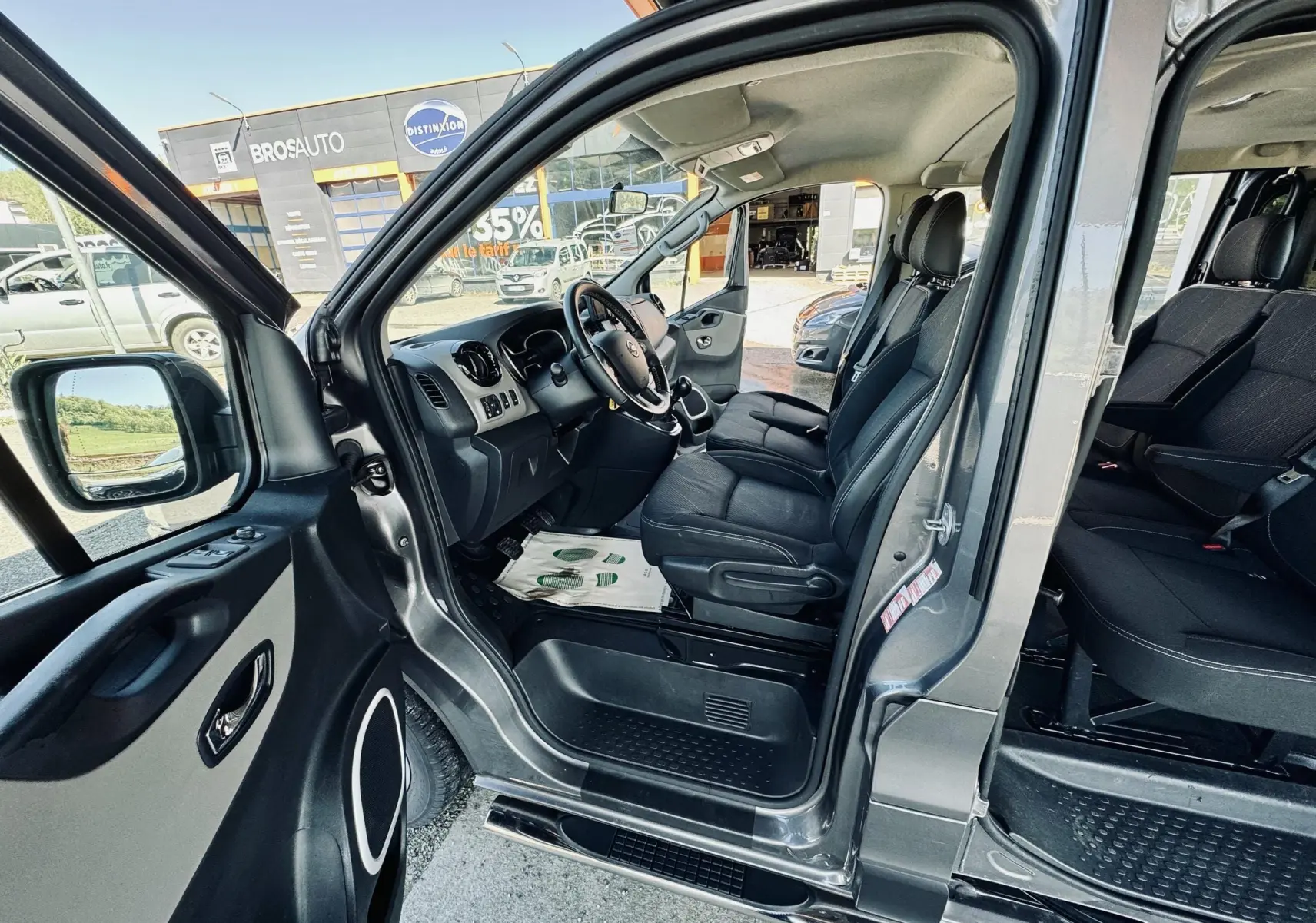 Vue intérieure côté conducteur du Nissan NV300 Combi gris, montrant les sièges avant et la porte ouverte.