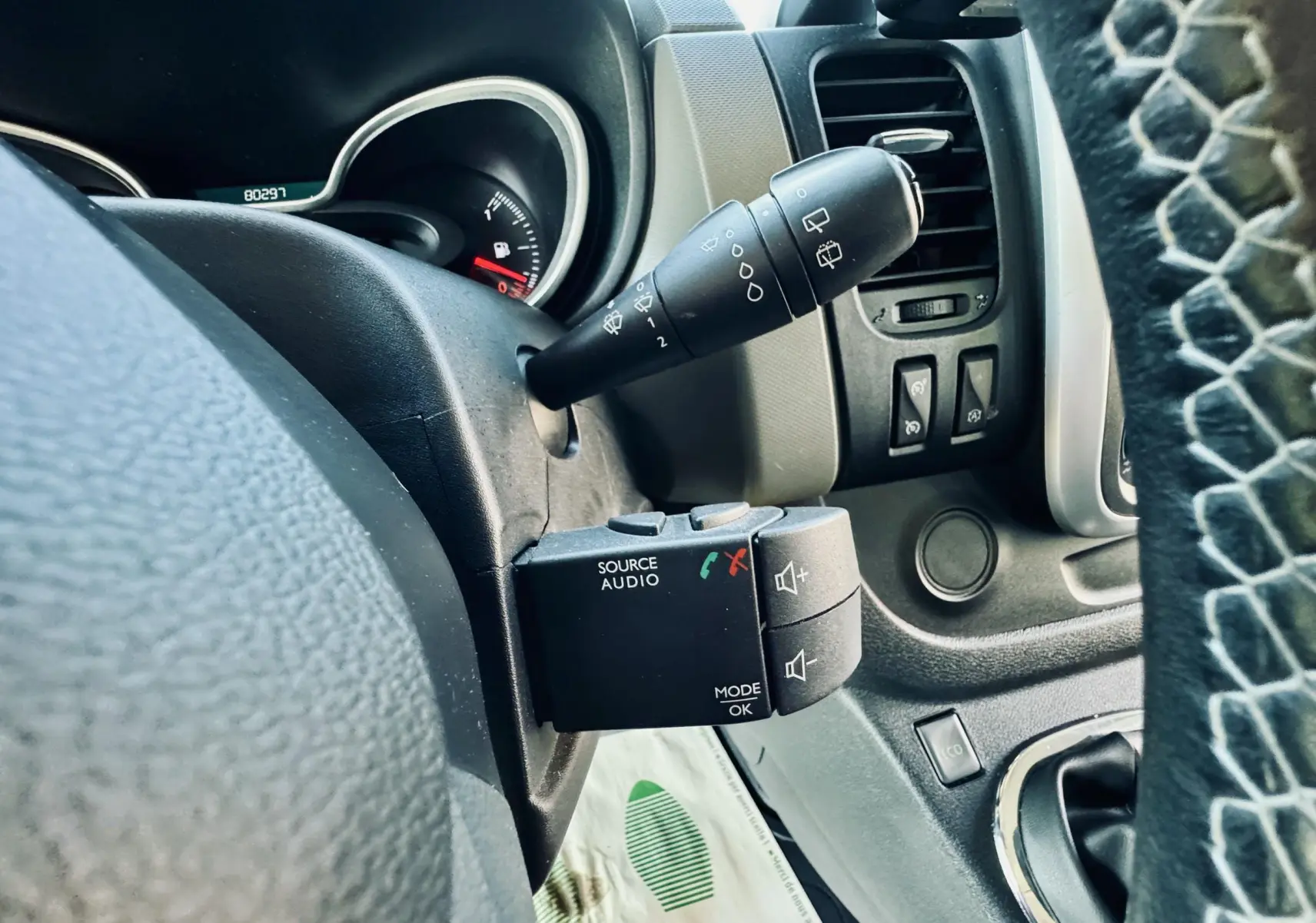 Gros plan sur la commande audio au volant du Nissan NV300 Combi gris, avec tableau de bord et aérateurs visibles.