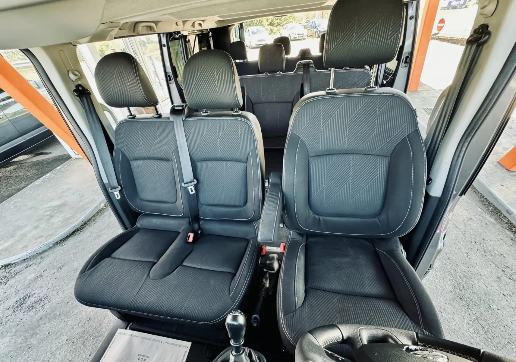 Vue intérieure avant du Nissan NV300 Combi gris, montrant les sièges en tissu noir et la boîte manuelle.