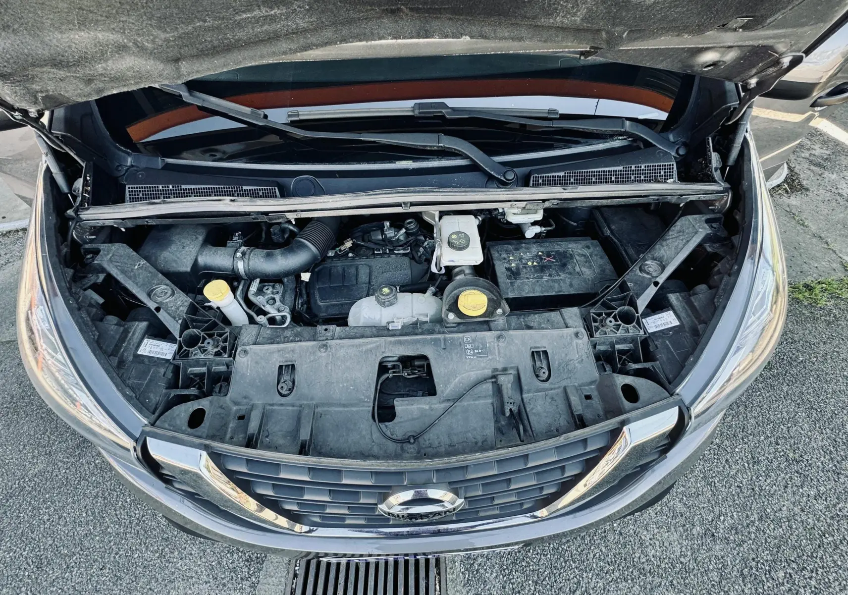 Vue plongeante sur le moteur gris d'un Nissan NV300 Combi 2018 avec capot ouvert, montrant la calandre avant.