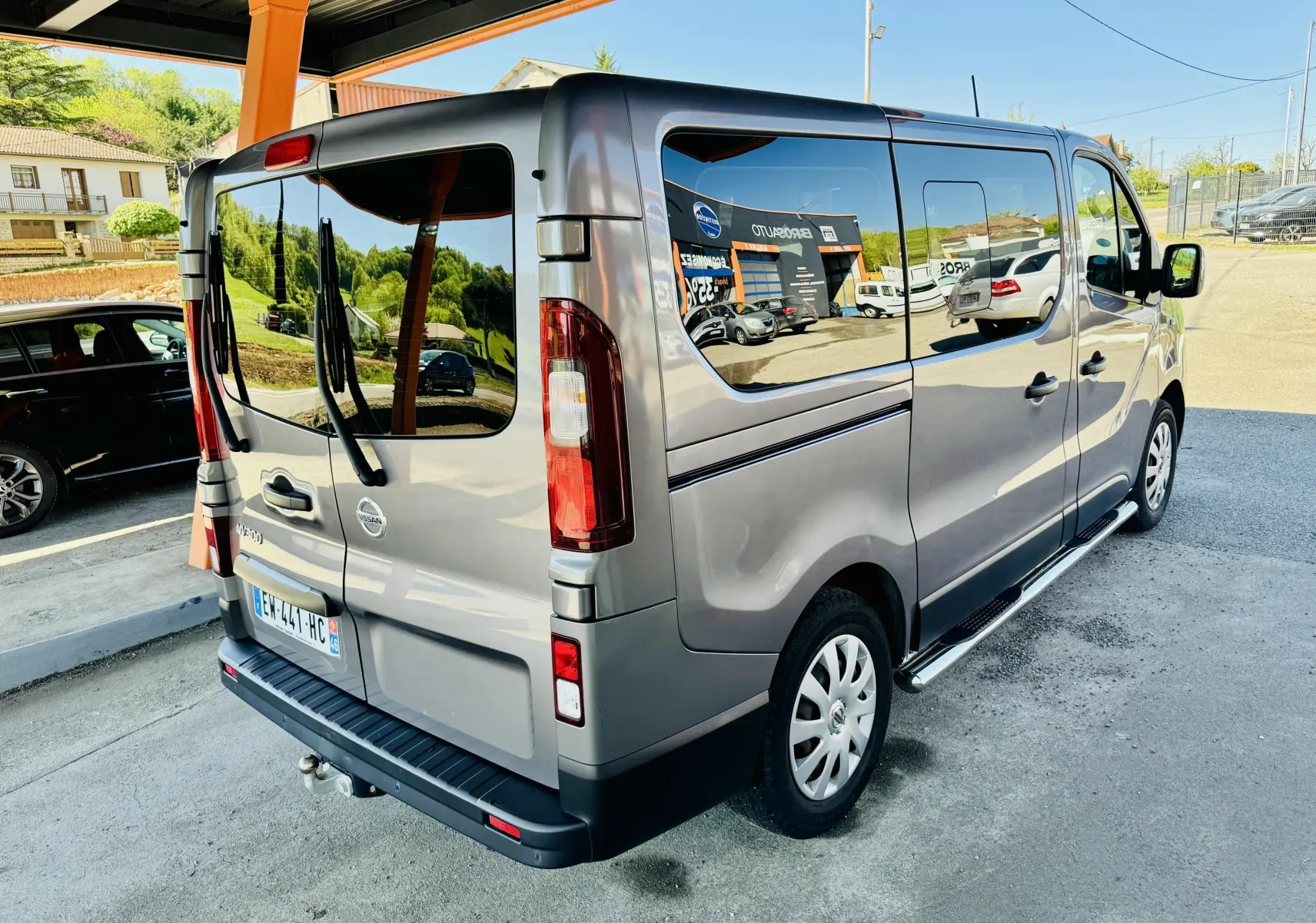 Vue 3/4 arrière droite d’un Nissan NV300 Combi gris métallisé avec vitres teintées et porte latérale coulissante visible.