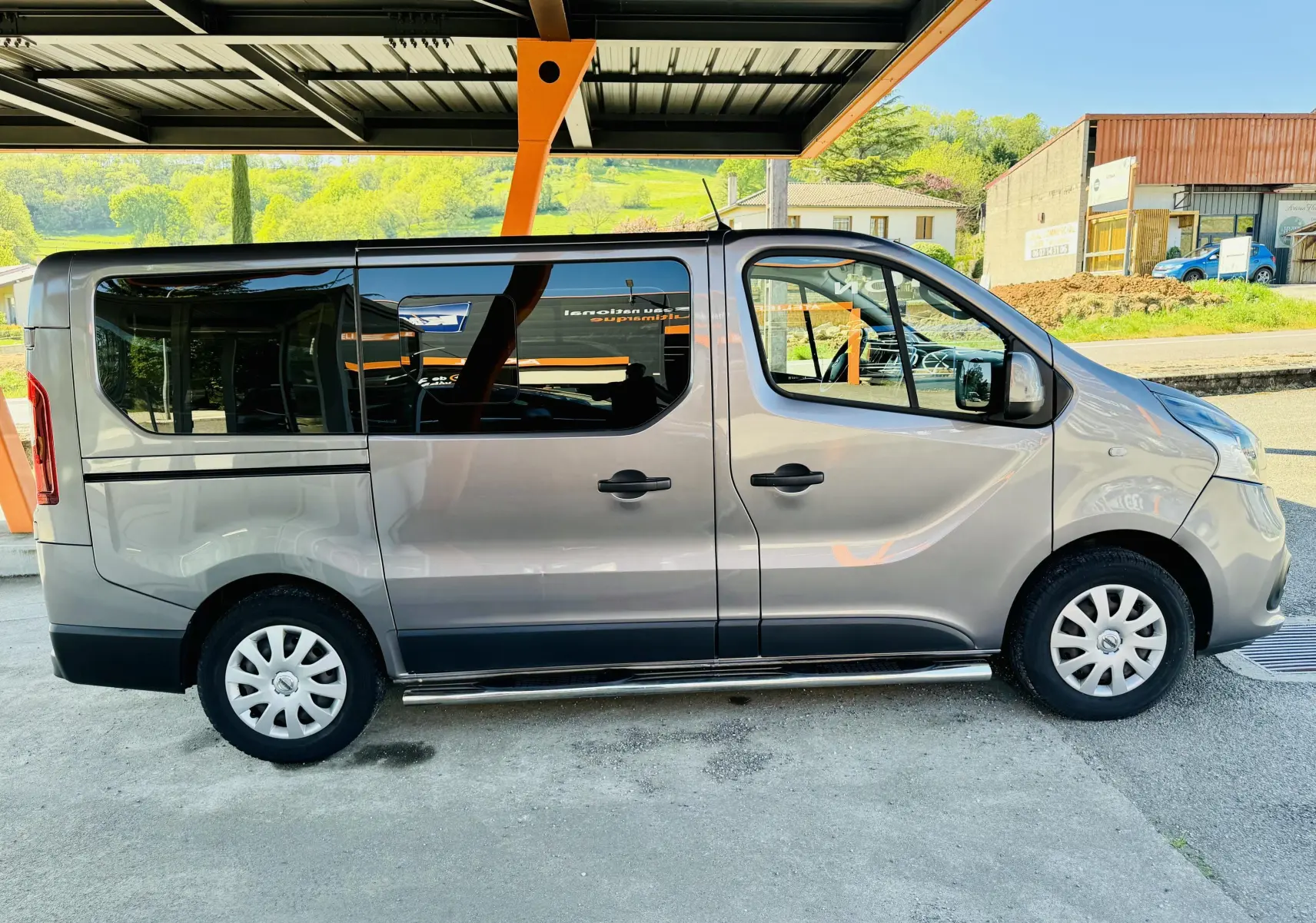 Profil droit d’un Nissan NV300 Combi gris 2018, avec vitres teintées et marchepied métallique sous les portes.