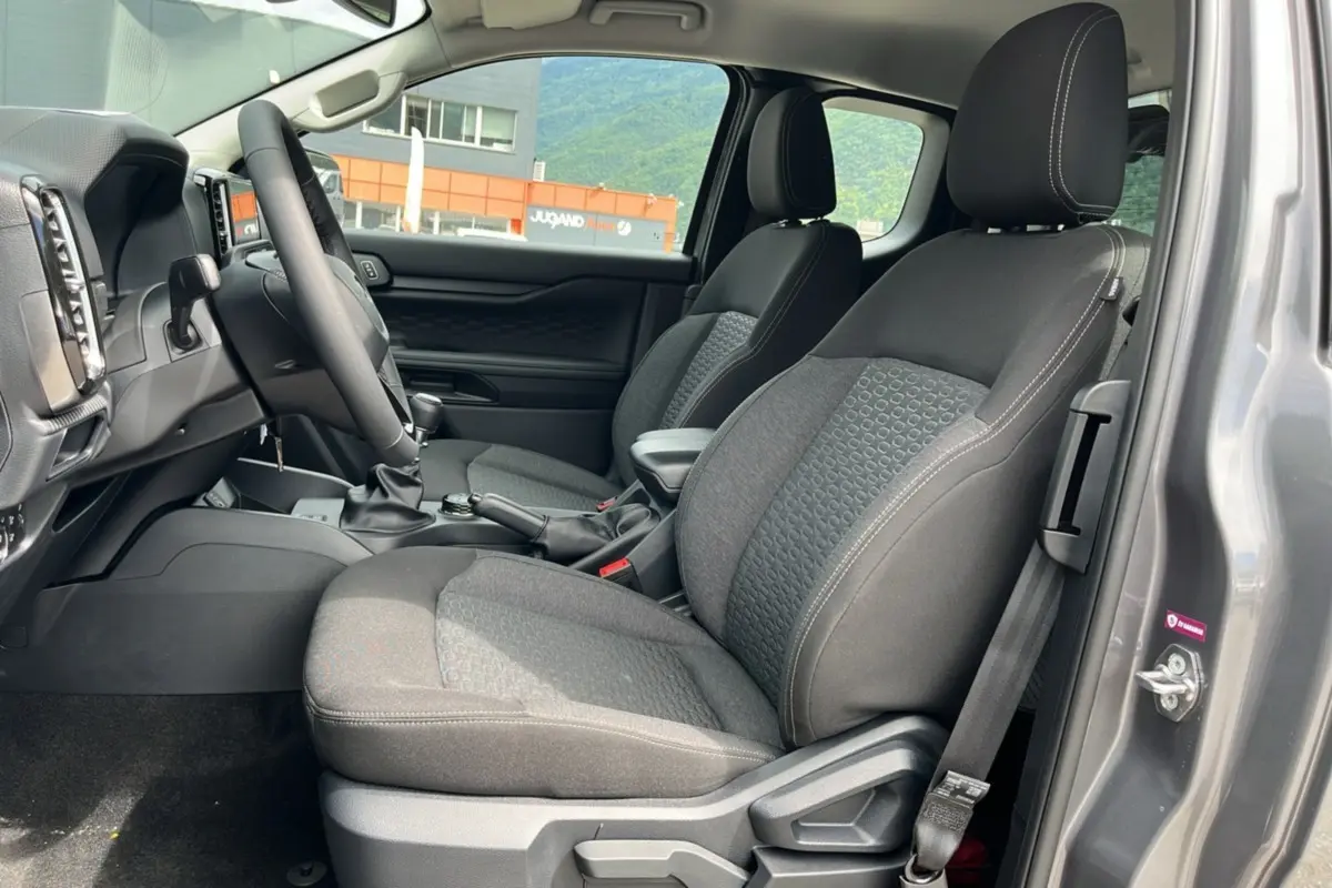 Vue intérieure côté conducteur du Ford Ranger gris carbone 2025, montrant les sièges avant en tissu et le volant multifonctions cuir.