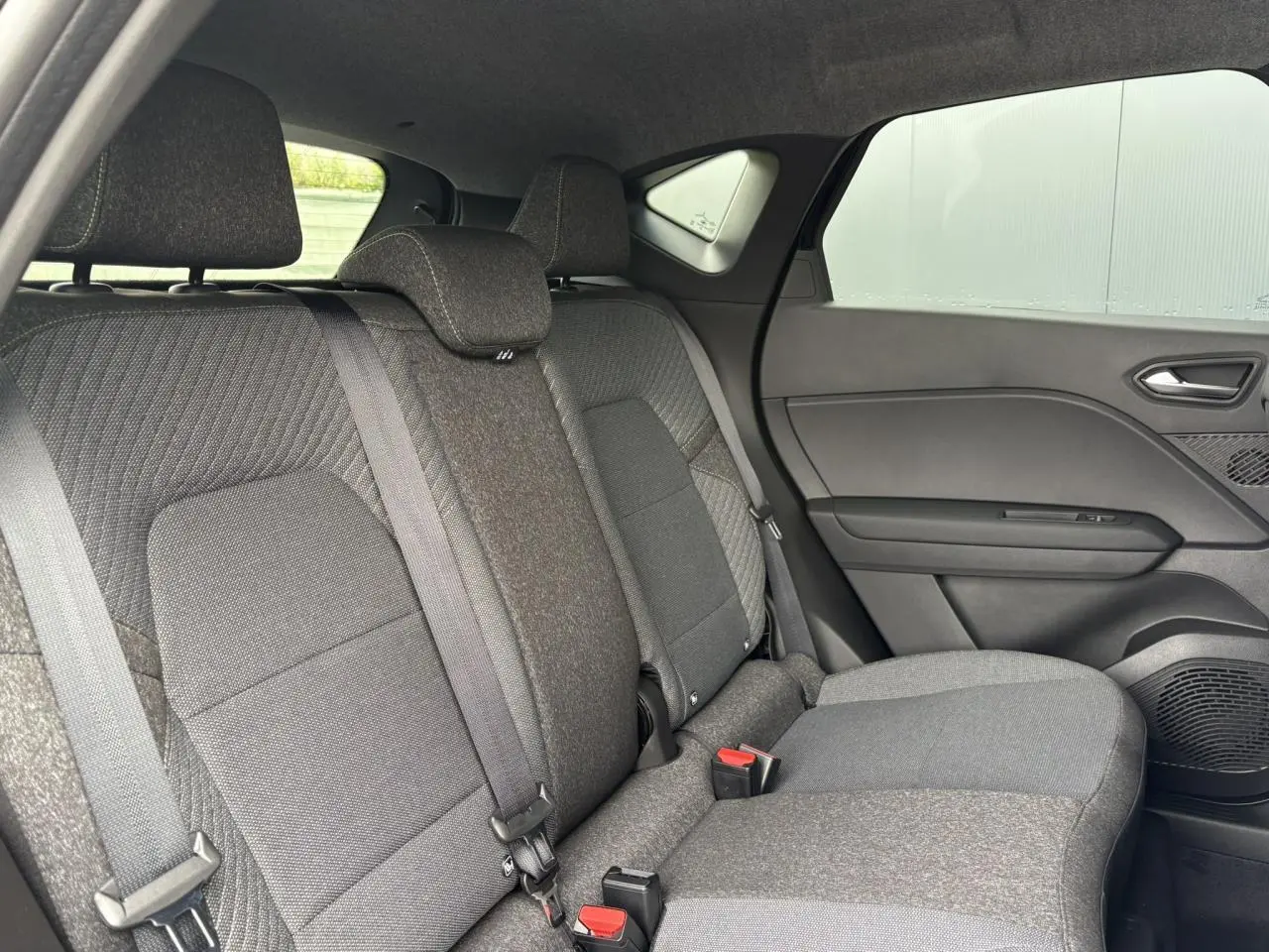Vue intérieure côté droit sur la banquette arrière grise du Renault Captur 2025 avec appuis-têtes et ceintures visibles.