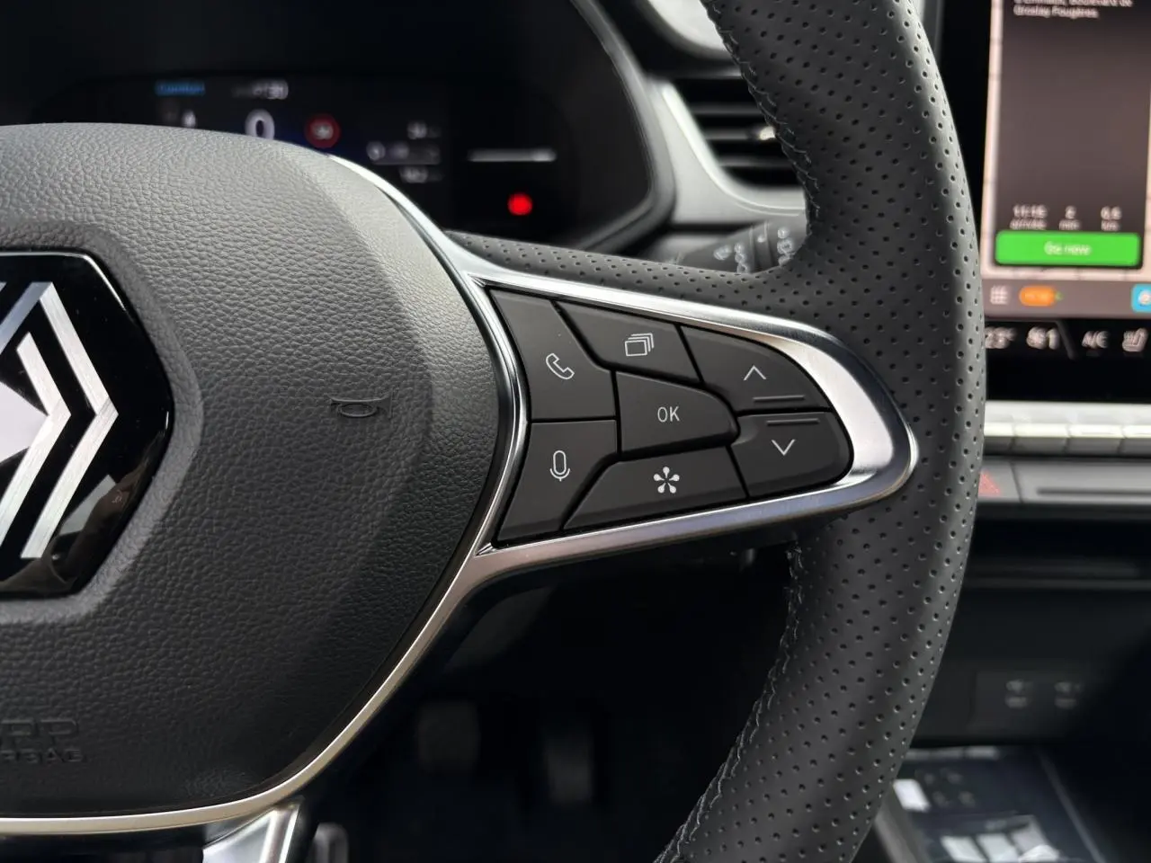 Gros plan sur le volant noir perforé du Renault Captur 2025 avec commandes multifonctions et écran tactile en arrière-plan.