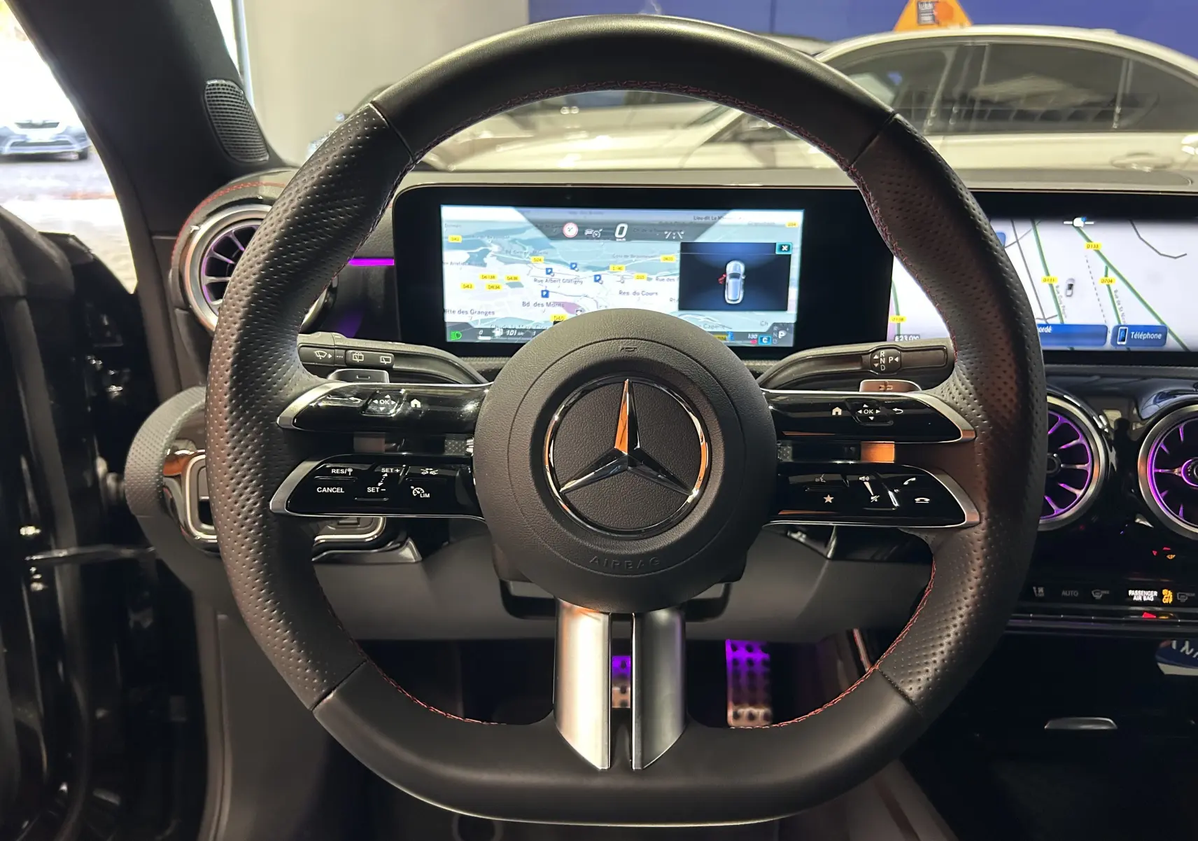 Vue centrée sur le volant noir perforé avec surpiqûres rouges du Mercedes Classe CLA Shooting Brake II 200D AMG 2024, tableau de bord numérique visible.